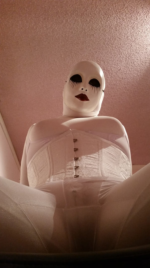 A photo of evil dolly clad all in white girdles, a white corset, and a white creepy doll mask.